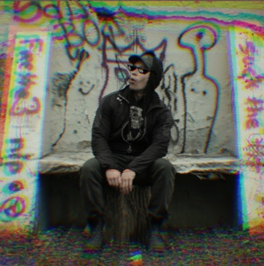 NOSAJ press shot: seated against a graffiti wall, rendered with an RGB glitch shift